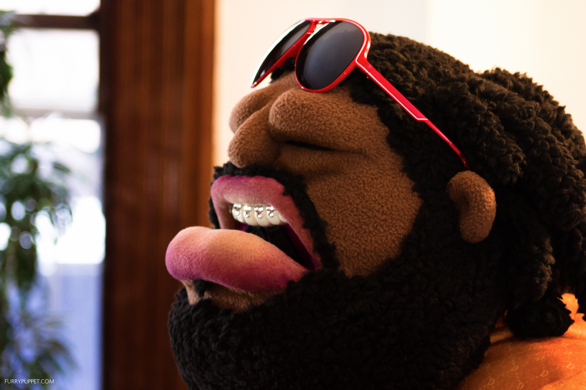 Custom character puppet by Furry Puppet Studio with black dreadlocks, red aviator sunglasses and braces